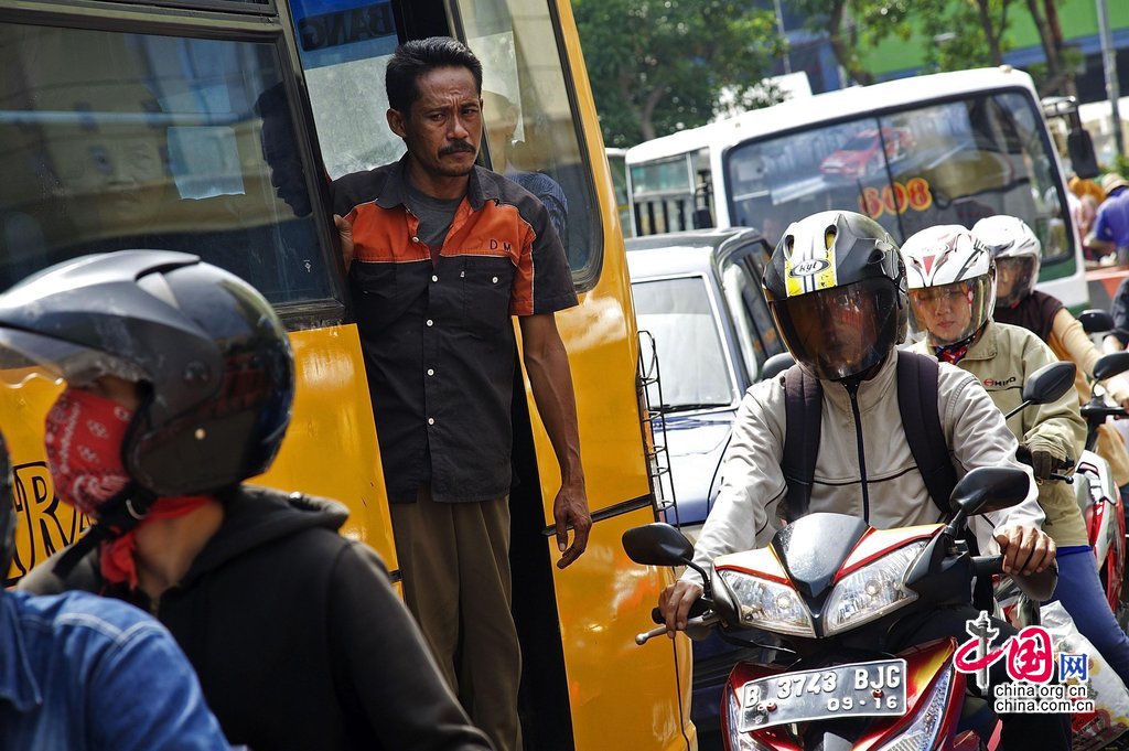 当地时间2013年12月19日，印尼雅加达，在严重的堵车中，摩托车从动弹不得的公交车旁驶过。