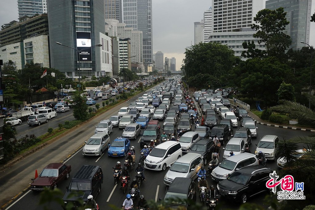 当地时间2013年12月19日，印尼雅加达，印尼民众行进在拥挤的道路上。交通专家警告称，雅加达或将在2014年部分时间面临完全的交通停滞。路上的车辆总数将会超过路面可承载数量，这也就意味着，如果大部分车在同一时间出现在道路上，或将会完全没有移动空间。