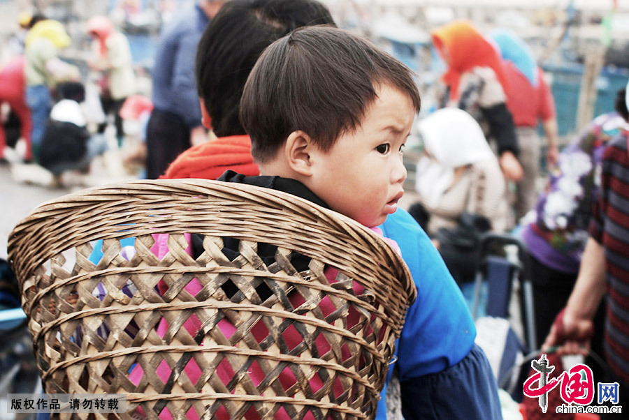 儘管已經漸漸融入當地漁民的生活，但移民們仍保留著自己的一些習慣。圖為2012年5月29日，一位漁民用背簍背著孩子在趕魚市。中國網圖片庫 王海濱/攝