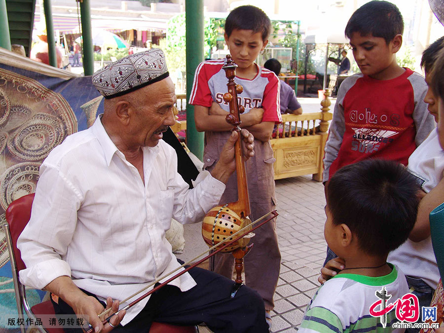喀什老城的一位老藝術家戴著花帽教小朋友艾捷克樂器。中國網圖片庫 孫繼虎/攝