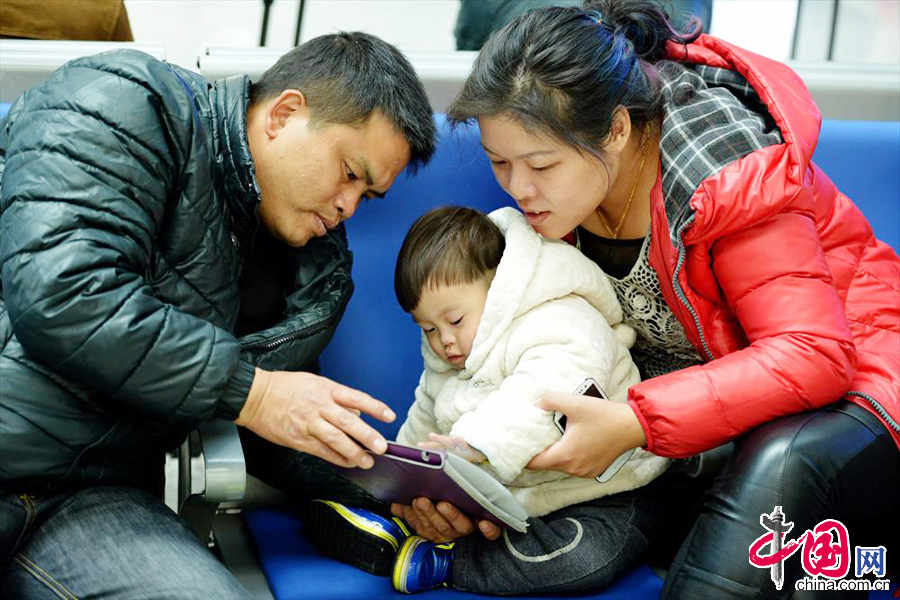 2014年01月16日，浙江省杭州市，父母與孩子在鐵路杭州東站候車大廳的座椅上一起玩ipad。 中國網圖片庫 龍巍攝影