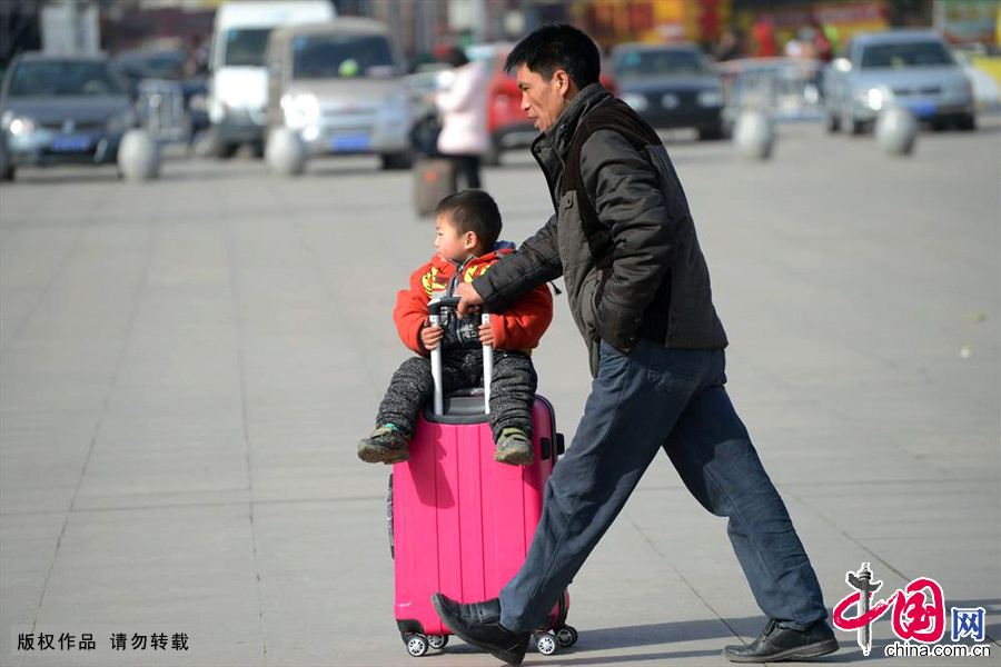 1月20日，安徽蚌埠火车站，一个孩子坐在行李箱上，爸爸推着赶往检票口。中国网图片库 高建业/摄