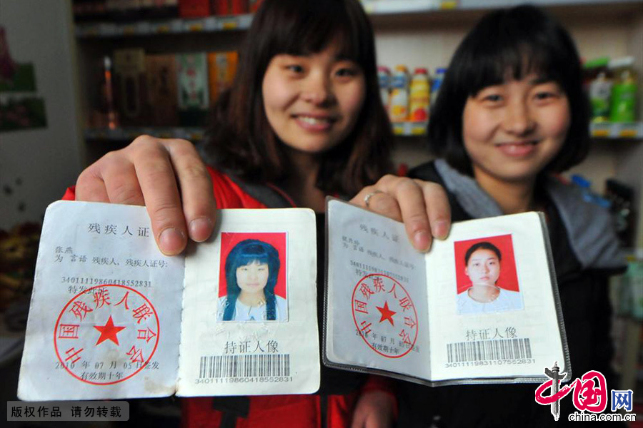姐妹俩展示自己的残疾证。她们总是微笑着面对每一天和每一个顾客，感染者周围的每一个人。在无声的世界里乐观努力的描绘着自己的人生。中国网图片库 葛传红/摄