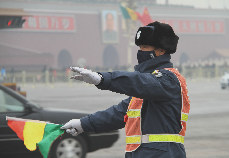 2月22日，北京全城被霧霾籠罩，當日，武警、特警、交通協管員、環衛員等戶外工作人員仍然堅守在自己崗位上。圖為天安門前交通協管員戴著口罩指揮車輛和行人。