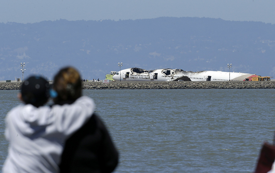 2013年7月6日，韩国亚洲航空公司一波音777客机在旧金山国际机场降落时机尾撞击跑道起点处一段海堤，继而起火，致死3名中国学生、致伤180多名乘客。这也是2009年以来在美国发生的首个致命客机事故。这是人们从远处眺望美国旧金山国际机场停机坪上的韩亚航空客机残骸（2013年7月8日摄）。新华社/美联