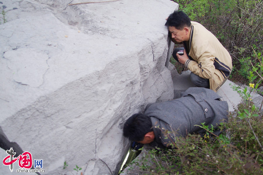 4月2日，李建国（右）在常平阻击战战场遗址关爷坡的巨石下找到抗日将士的遗骨。