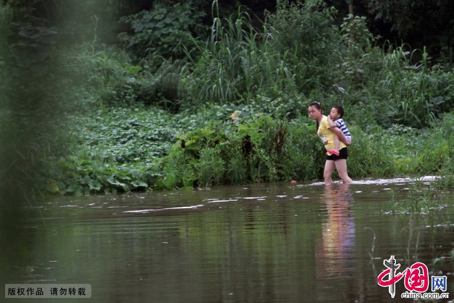 6月19日，在福建省厦门市海沧区后坑村，一位村民背着小孩在积水严重的路段涉水出行。