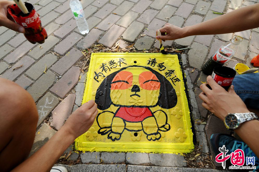 2014年6月24日，兩名學生在井蓋上塗鴉可愛的卡通狗形象。 中國網圖片庫 王海濱攝影