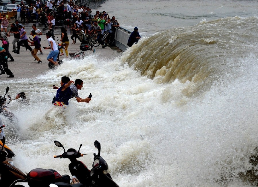 2014年8月15日，杭州，钱江潮水在杭州九溪江堤掀起巨浪，瞬间打湿了观潮者，一位淡定哥手持手机在潮水中拍摄。