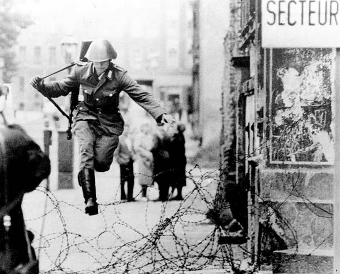 1961年8月15日，一名东德士兵穿过贝尔瑙尔大街上的铁丝网逃亡西德，那里有他的亲人和“自由”。