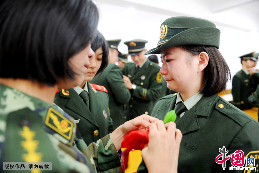 图为11月23日，在警徽告别仪式上，武警福建总队通信站留队战友为退伍女兵卓珊珊（右）卸下警衔。