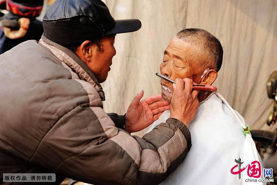  2014年1月11日，山东青岛，大村镇年集上理发师在给顾客刮胡须。