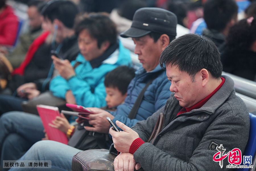  2015年2月8日，上海虹桥火车站候车厅，几名乘客正在低头看着手机等电子设备。随着科技不断的发展，智能手机、PAD、电脑等越来越多的电子产品成了我们生活中的必需品，在虹桥火车站候车厅，虽然正值春运，却少了以往的喧嚣声，随处可看到“恋屏族”。中国网图片库 王亚东/摄　