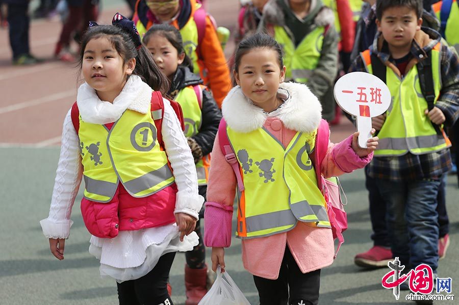 3月11日，河南郑州一小学的学生们穿着黄色的荧光马甲走出校门，穿过马路放学回家。中国网图片库 杨正华/摄