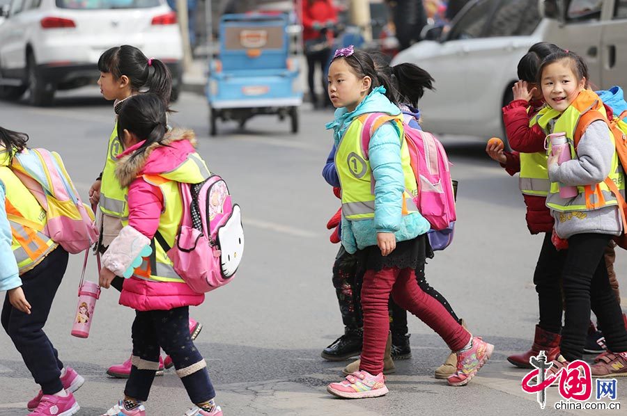 3月11日，河南郑州一小学的学生们穿着黄色的荧光马甲走出校门，穿过马路放学回家。中国网图片库 杨正华/摄