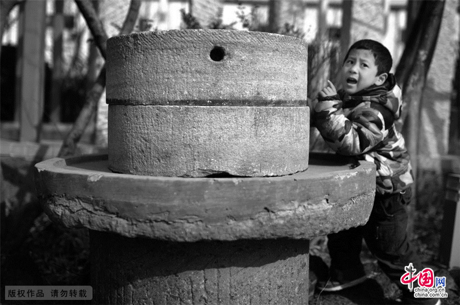 2015年3月14日，海草房前，一名儿童在一处旧石磨边上玩耍。中国网图片库 王海滨/摄