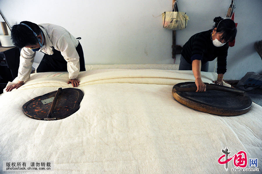王定民与屋子李开珍在碾压粘板，让网线与棉絮融合。中国网图片库 饶国君/摄