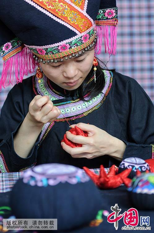  一名壮族姑娘在制作“麽乜”饰物。如今，人们在传统“麽乜”工艺的基础上，融入百色壮族本土蜡染、土布、壮锦、竹编等丰富多彩的民族文化资源和现代生活元素。中国网图片库 韦万忠 摄