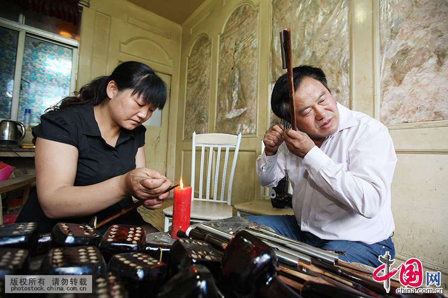 卢俊军在测听加工簧片发音，妻子刘英（左）帮助他将簧片焊装在笙管上。中国网图片库 胡卫国 摄