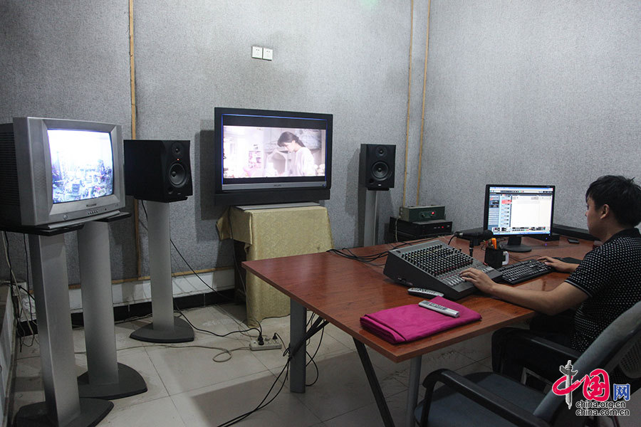  在旁邊的錄音室裏，錄音師正在忙碌著。墻上的兩台顯示屏，分別可以看到擬音棚內的實時景象和需要擬音的畫面，錄音師通過話筒進行指導。中國網記者 倫曉璇 攝 