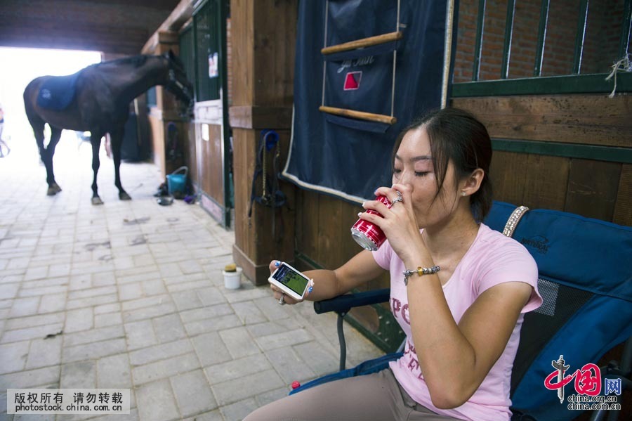 休息的時間，田雨也不會閒著，她利用比賽間隙邊喝可樂邊看馬術比賽視頻。中國網圖片庫 蘭洋攝
