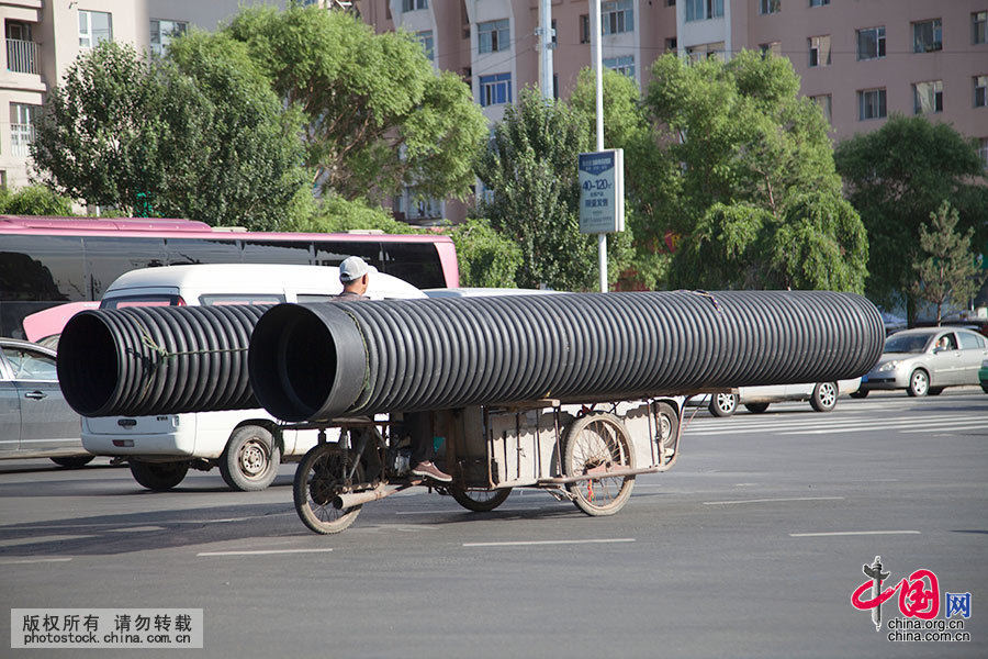  2015年6月19日，吉林省吉林市一男子騎著一輛改裝的倒三輪摩托車載著兩根直徑一米多，七八米長的管子行駛在解放大路上，只露個腦袋勉強看路，晃晃悠悠的讓人為其安全捏把汗。中國網圖片庫 朱萬昌 攝