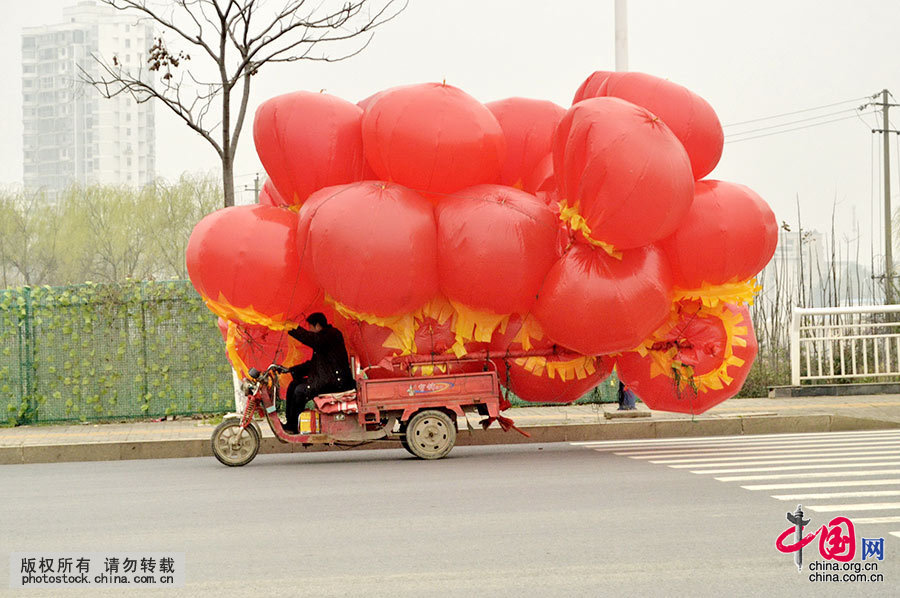  2015年3月10日上午，湖南常德市紫緣路上，一輛滿載氫氣球的電動三輪車在車流中搖晃前行，過往車輛都避而遠之，路口執勤交警當即將其攔截並對其行為進行了查處。中國網圖片庫 陳自德 攝