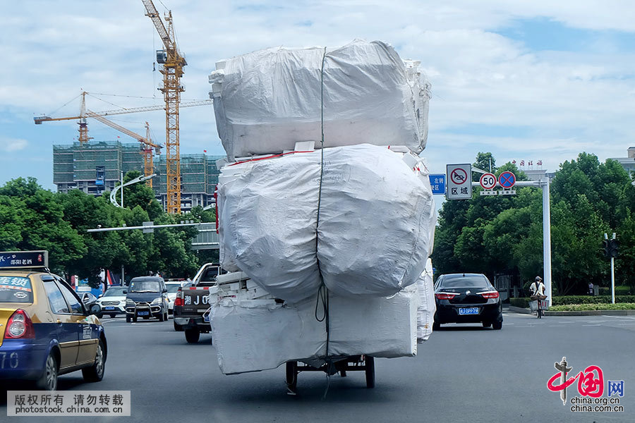  8月5日上午，湖南常德市紫淩路上，一輛三輪車拖著超高超長的貨物前行，本身不大的三輪車成了一輛“貨車”，過往車輛駕駛人驚呼“馬路雜技”，路口執勤交警當即將其攔截對其行為進行了查處。中國網圖片庫 陳自德 攝