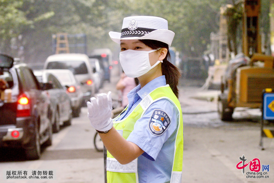  2014年9月23日早晨，一名女交警正在光荣路口戴口罩执勤，根据公安部允许在空气严重污染时，交警可以戴口罩执勤的相关精神，当日，该市交警首推戴口罩执勤。中国网图片库 陈自德摄