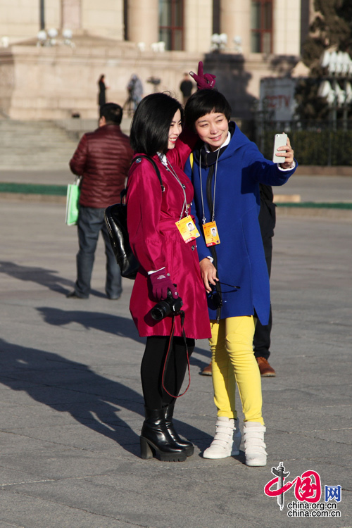 2014年兩會，一位身穿深紅上衣女記者與同行在人民大會堂前合影。中國網 鄭亮 攝