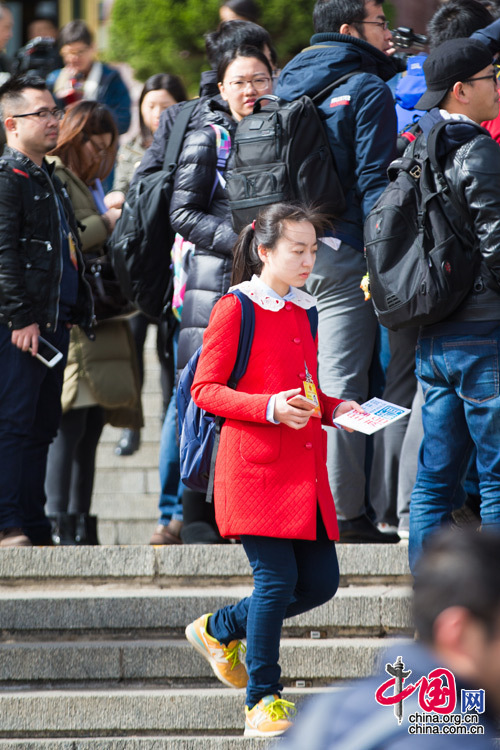 2016年兩會，人民大會堂前，身穿娃娃領紅色上衣的一名女記者匆匆走過人群。中國網 鄭亮 攝