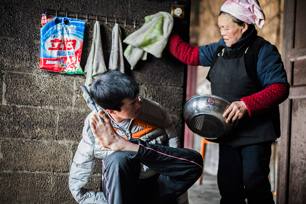 陳茲方（左）在家中梳理頭髮準備與客戶約談，母親在一旁準備為他做早飯（3月2日攝）。