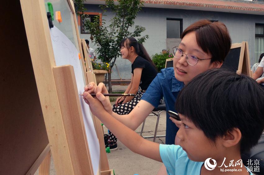 活动现场，大学生志愿者也参与其中，手把手教北京太阳村的孩子画画。人民网尹星云 摄