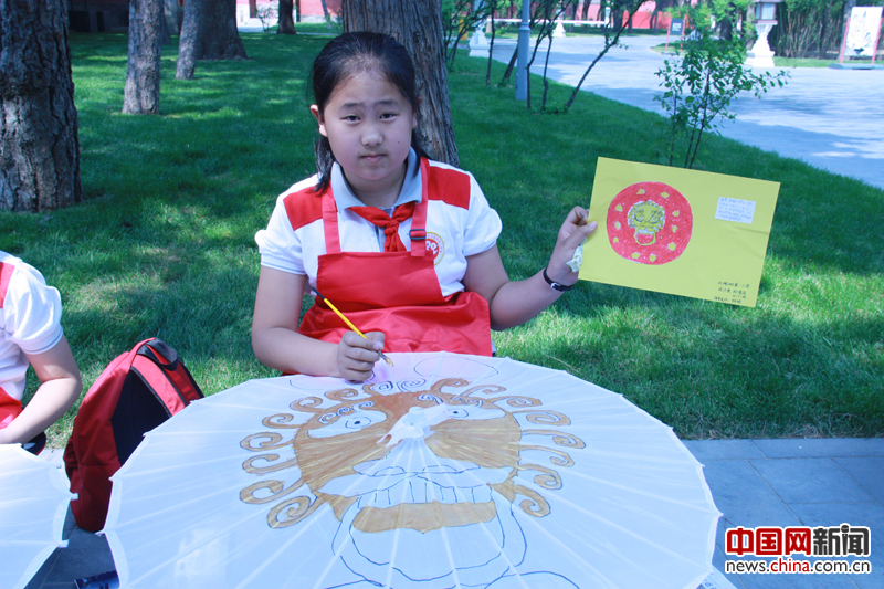  5月18日，在故宫武英门外，北京市海淀区双榆树第一小学的40名学生在进行“故宫元素彩绘伞”活动。图为四年级学生郝德岩展示她设计的彩绘伞。 摄影 中国网 苏向东