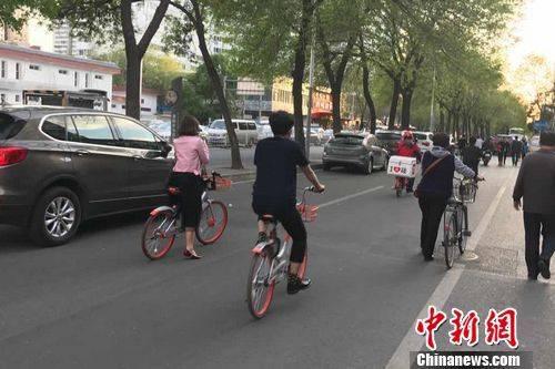 北京街道上正在骑共享单车的人。程春雨摄