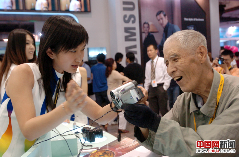 2005年，工作人员向74岁的李春生老人介绍一款新型摄录机。当日，第八届中国北京国际科技产业博览会在京开幕。来自世界29个国家和地区的政府和专业组织、世界500强企业、世界著名金融投资机构、工商企业界人士将分别参加为期5天的展览和各种科技经贸交流活动。  照片提供 南云