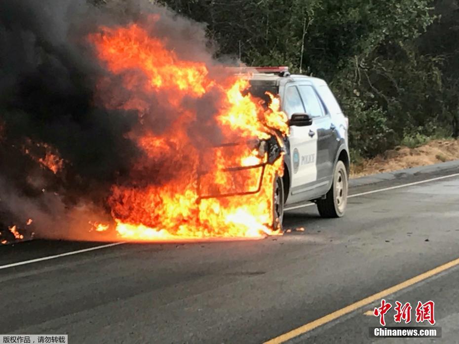 图为加州圣伊内斯154号高速公路上，一辆警车被山火点燃。