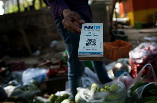 资料图片：2017年4月12日，在印度新德里街头，一名蔬菜摊主手持Paytm二维码接受电子支付。印度Paytm在支付宝母公司蚂蚁金服的支持下，已经成为印度最大的移动支付平台。新华社记者 毕晓洋 摄