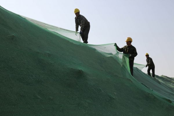 资料图片：2017年11月5日，在山东省滨州市博兴县一处建筑工地，建筑工人在施工现场的土方上覆盖密目网。新华社发