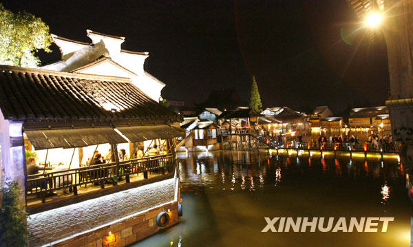 Photo : le 26 avril, des touristes contemplent les illuminations nocturnes de la tour Bailian du site touristique de Xizha à Wuzhen. 