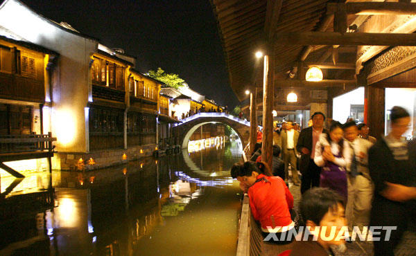Photo : le 26 avril, des touristes contemplent les illuminations nocturnes de la tour Bailian du site touristique de Xizha à Wuzhen. 