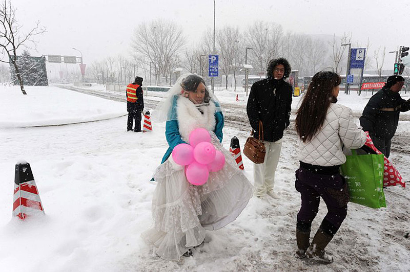 Un couple attend sa voiture sous la neige après avoir pris des photos de mariage. 