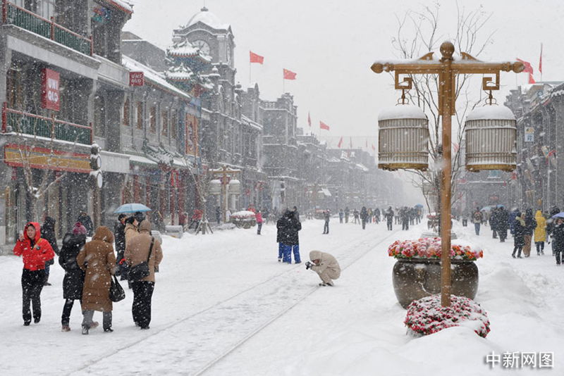 Les promeneurs arpentent la rue enneigée de Qianmen. 