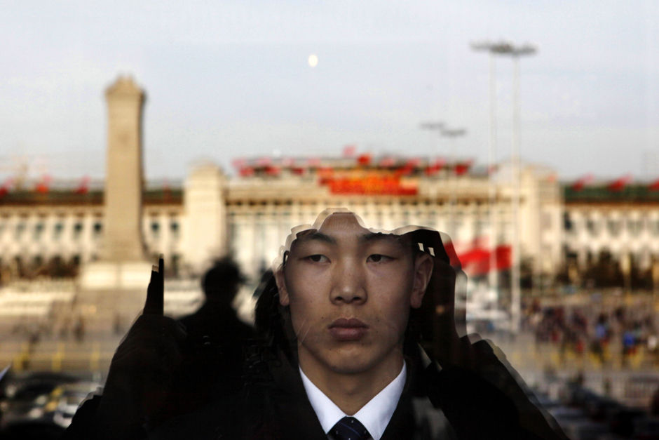 Dans le Grand Palais du Peuple, un gardien observe par une fenêtre donnant sur la place Tian'anmen, où les drapeaux rouges flottent au vent.