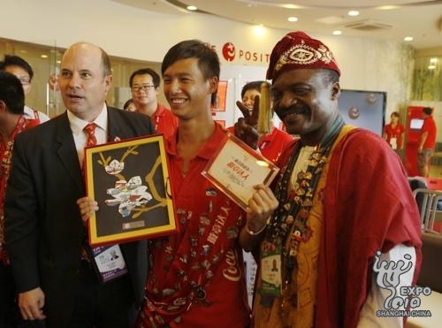 Virgile Ahouandjinou, « roi du pin's », et David Brooks, le chef d'exploitation du groupe Coca-cola, prennent une photo avec le « pin's en édition limitée de l'Expo »
