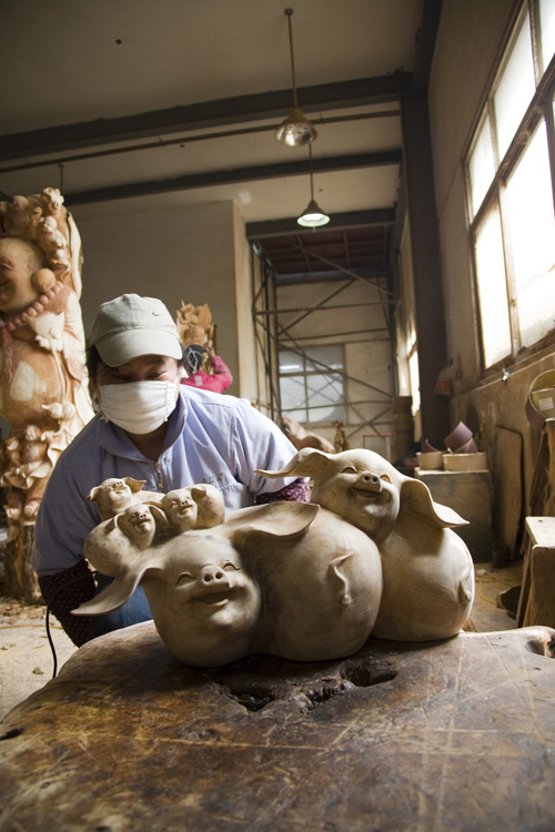 Une femme ponce et polit des cochons sculptés.