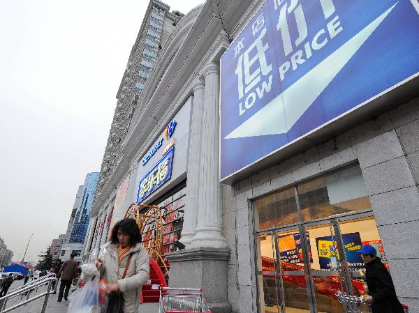 Le 27 janvier, des clients sortent du magasin Carrefour de Guangqumen à Beijing, après avoir fait leurs achats, sous un panneau publicitaire qui porte les mots « les mêmes produits moins chers ».