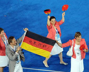 Das Bild zeigt, wie die deutsche paralympische Delegation ins Vogelnest kommt. Auf einer Deutschlandfahne steht '北京，你好!' (Hallo, Beijing!) geschrieben.