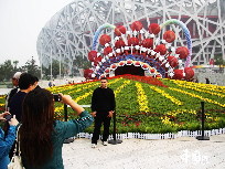 Touristen machen Fotos vor einer riesigen Dekoration beim Nationalstadion, dem Vogelnest, in der chinesischen Hauptstadt Beijing. Der Olympiapark, in dem sich das Vogelnest befindet, wurde zur Feier des 60. Jahrestags der Gründung der Volksrepublik China für den 1. Oktober in Schale geworfen. [Foto von Hu Junfeng]