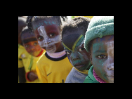 Kinder, die sich die Gesichter in den Farben verschiedener bei der Fußball-WM antretender Länder geschminkt haben, stehen in einem Gemeinschaftszentrum in Soweto in Johannesburg Schlange, um sich eine Nachbildung des WM-Pokals anzusehen (4. Juni 2010). [China Daily/Agenturen]